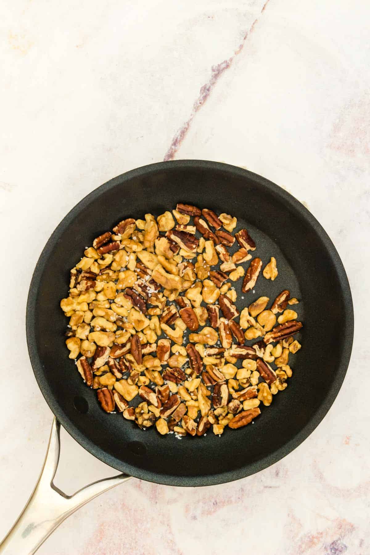 A mixture of walnuts and pecans in a small skillet.