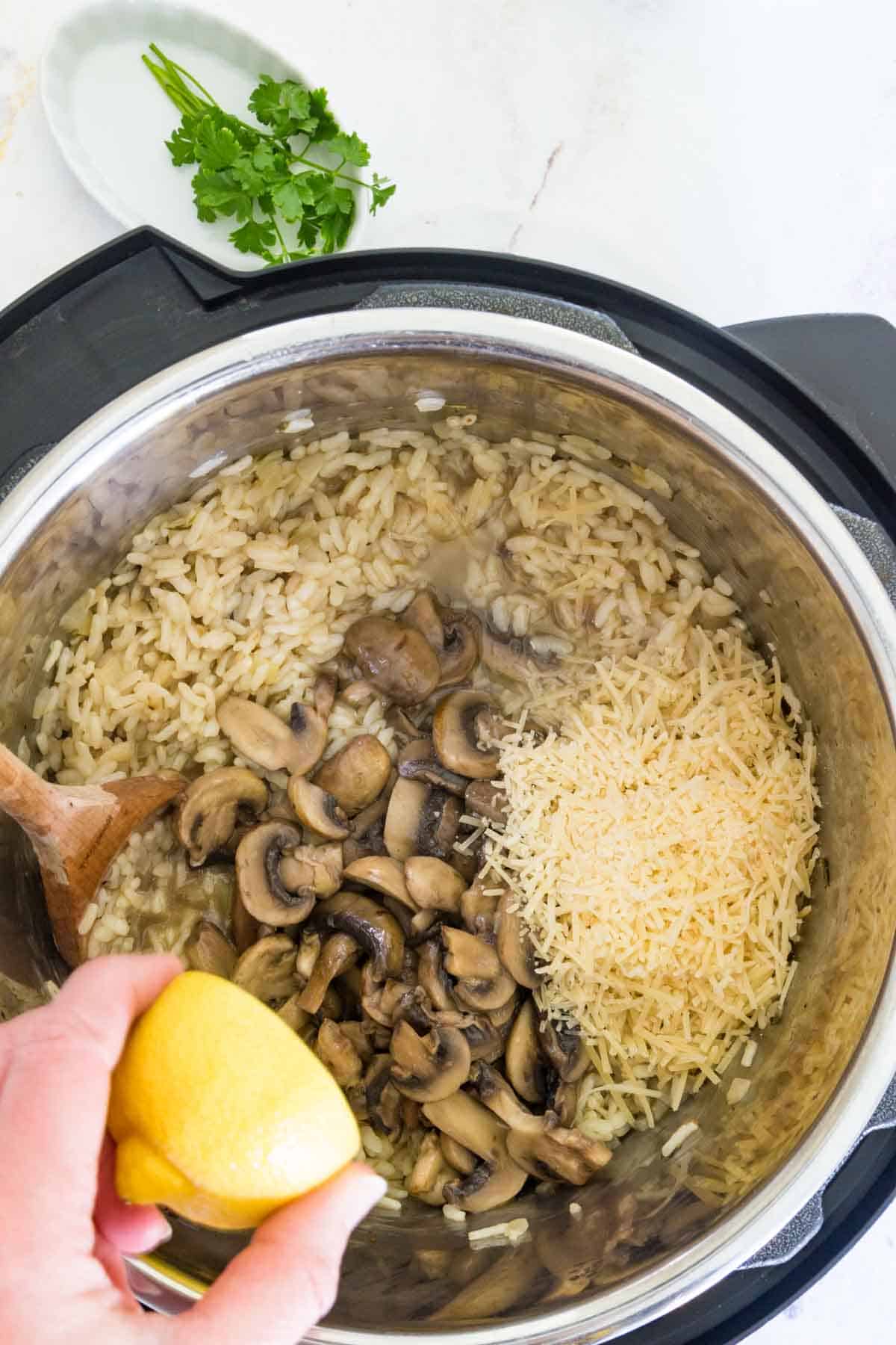 A hand squeezes a lemon over risotto with mushrooms and parmesan inside the instant pot.