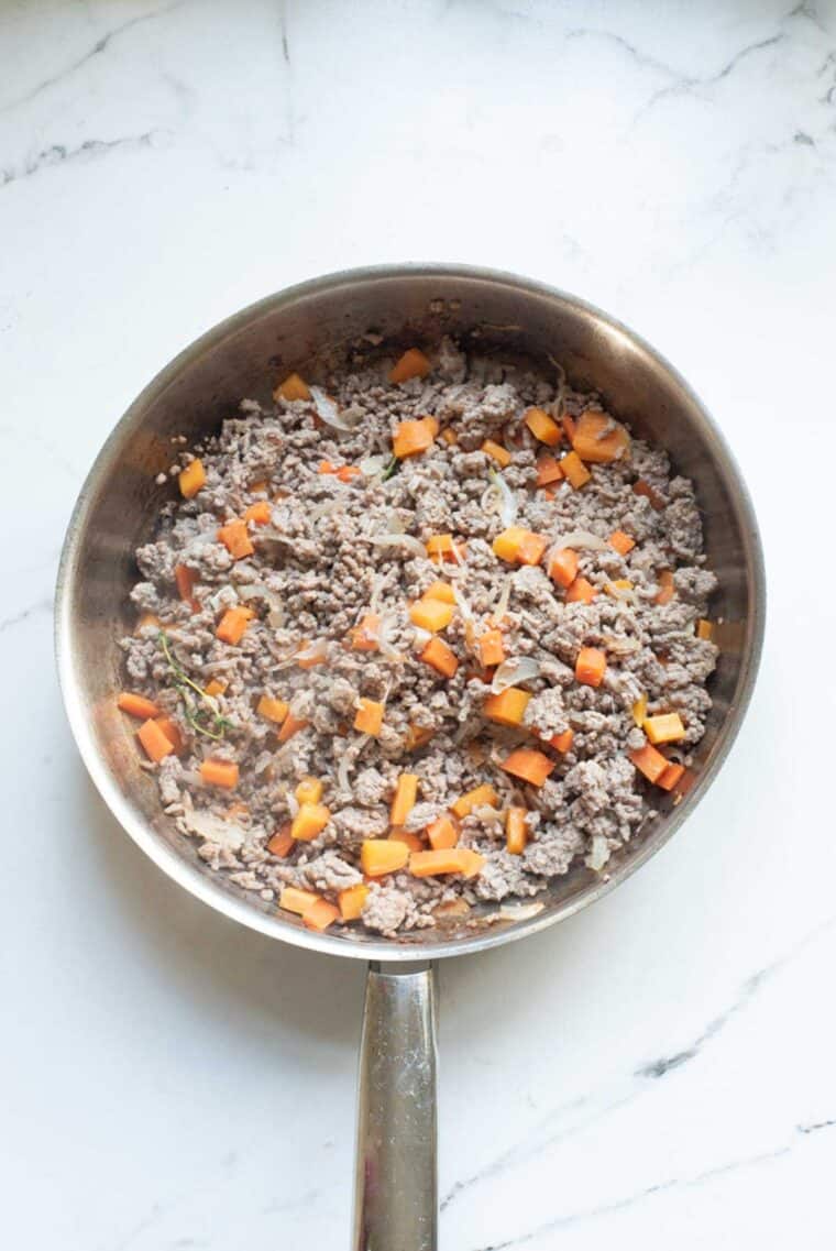 Veggies sauteing with ground beef as it cooks in a large skillet.