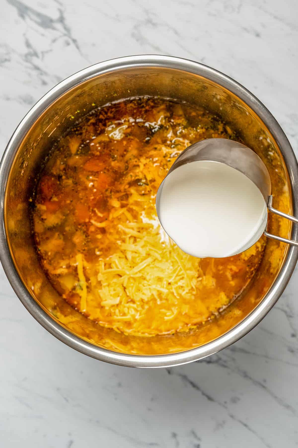 Half-and-half and shredded cheese is added into soup ingredients inside an Instant Pot.