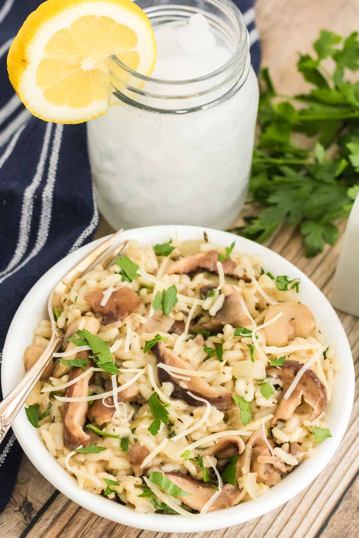 Overhead view of a bowl of Instant Pot mushroom risotto next to a glass of lemonade garnished with a lemon wedge.