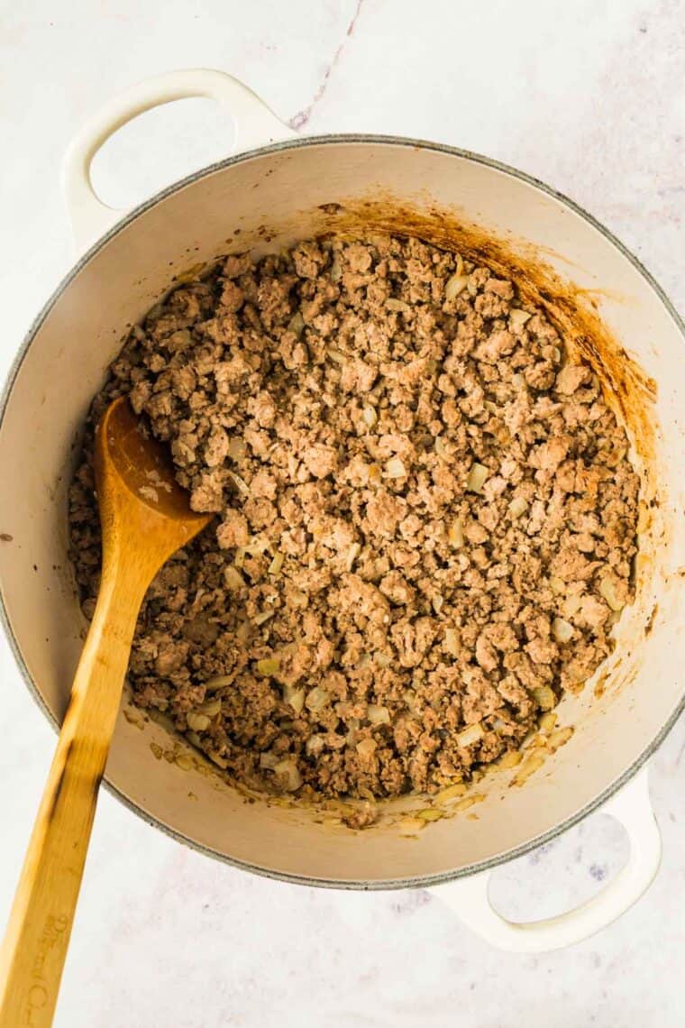 Browned sausage and ground beef in a Dutch oven with a wooden spoon.