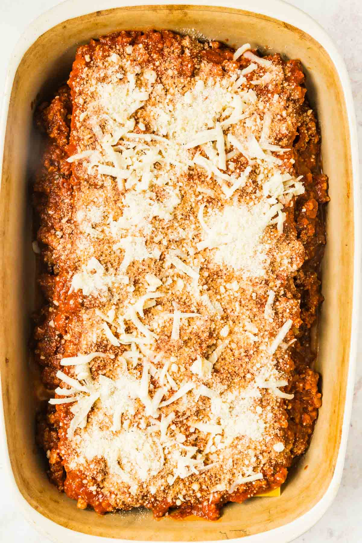 A fully assembled but unbaked gluten free lasagna in a baking pan topped with mozzarella and parmesan cheese.
