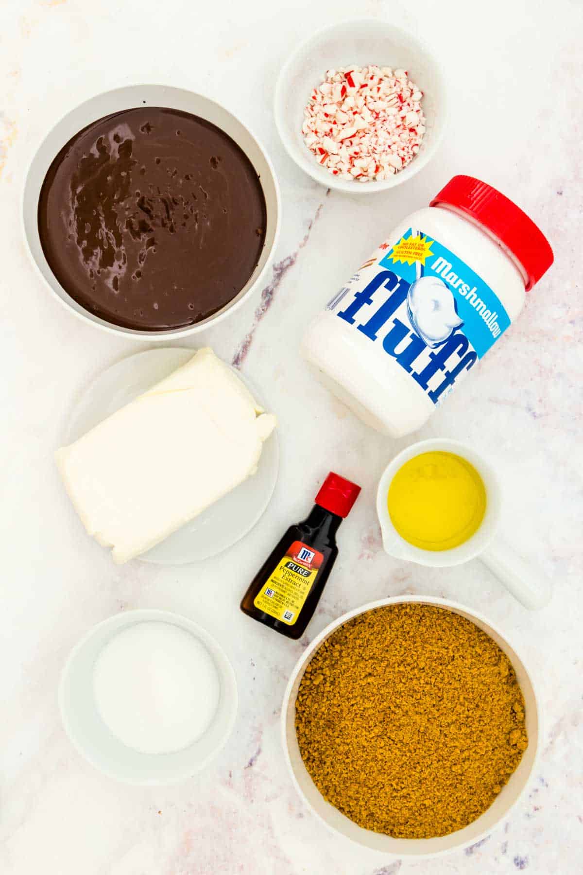 Ingredients to make no-bake chocolate peppermint cheesecake in bowls on a marble countertop.