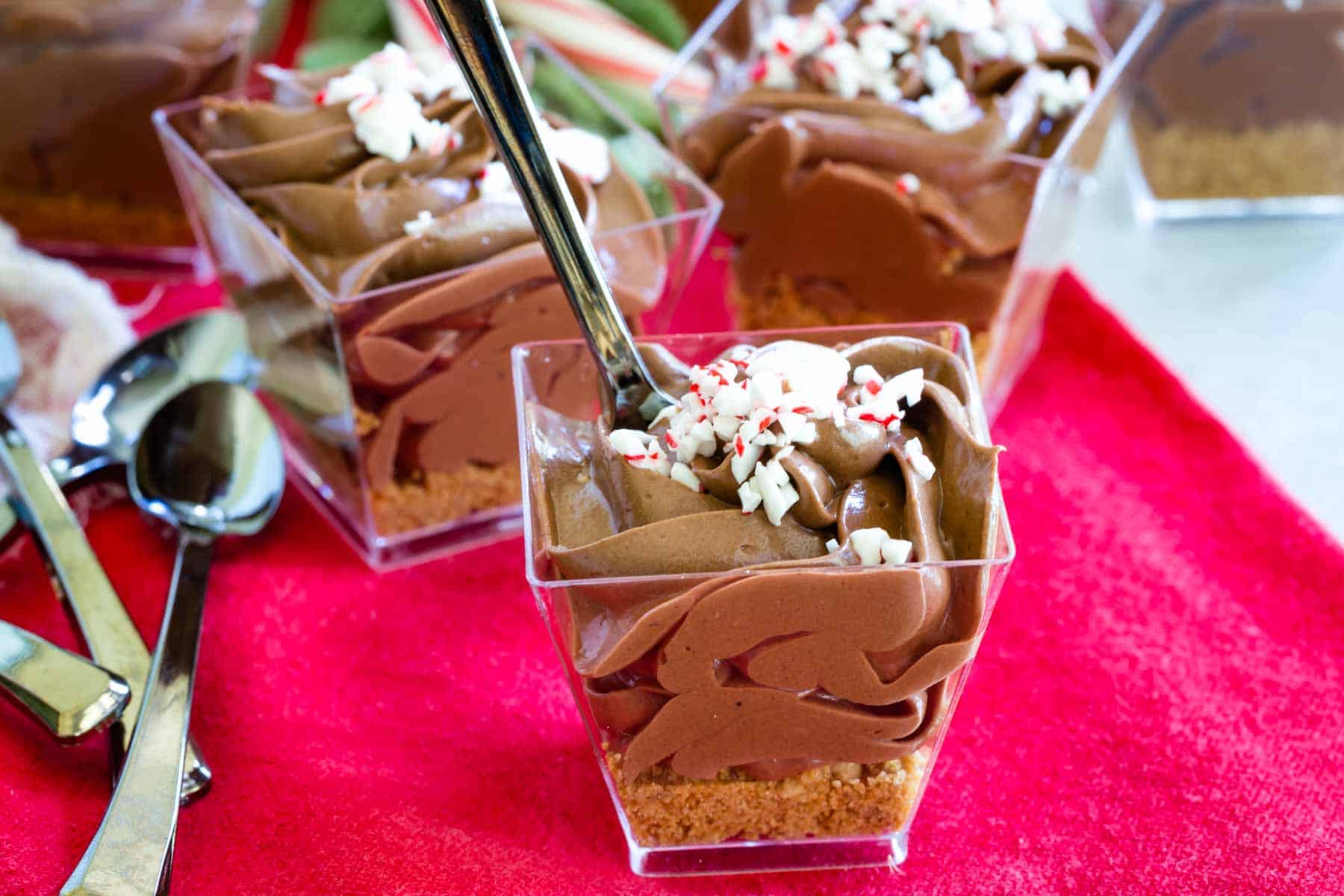Mini chocolate peppermint cheesecakes on a red cloth napkin with a pile of mini spoons.