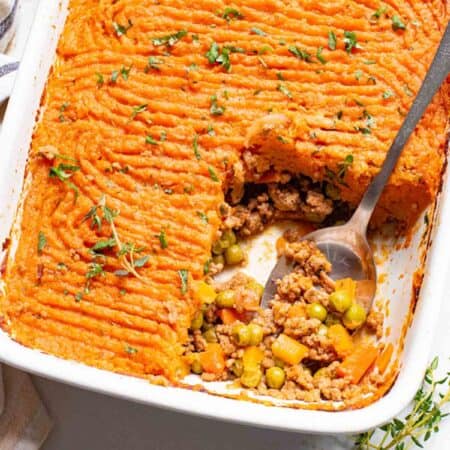 Overhead view of a metal spoon scooping a serving of sweet potato shepherd's pie from a casserole dish.