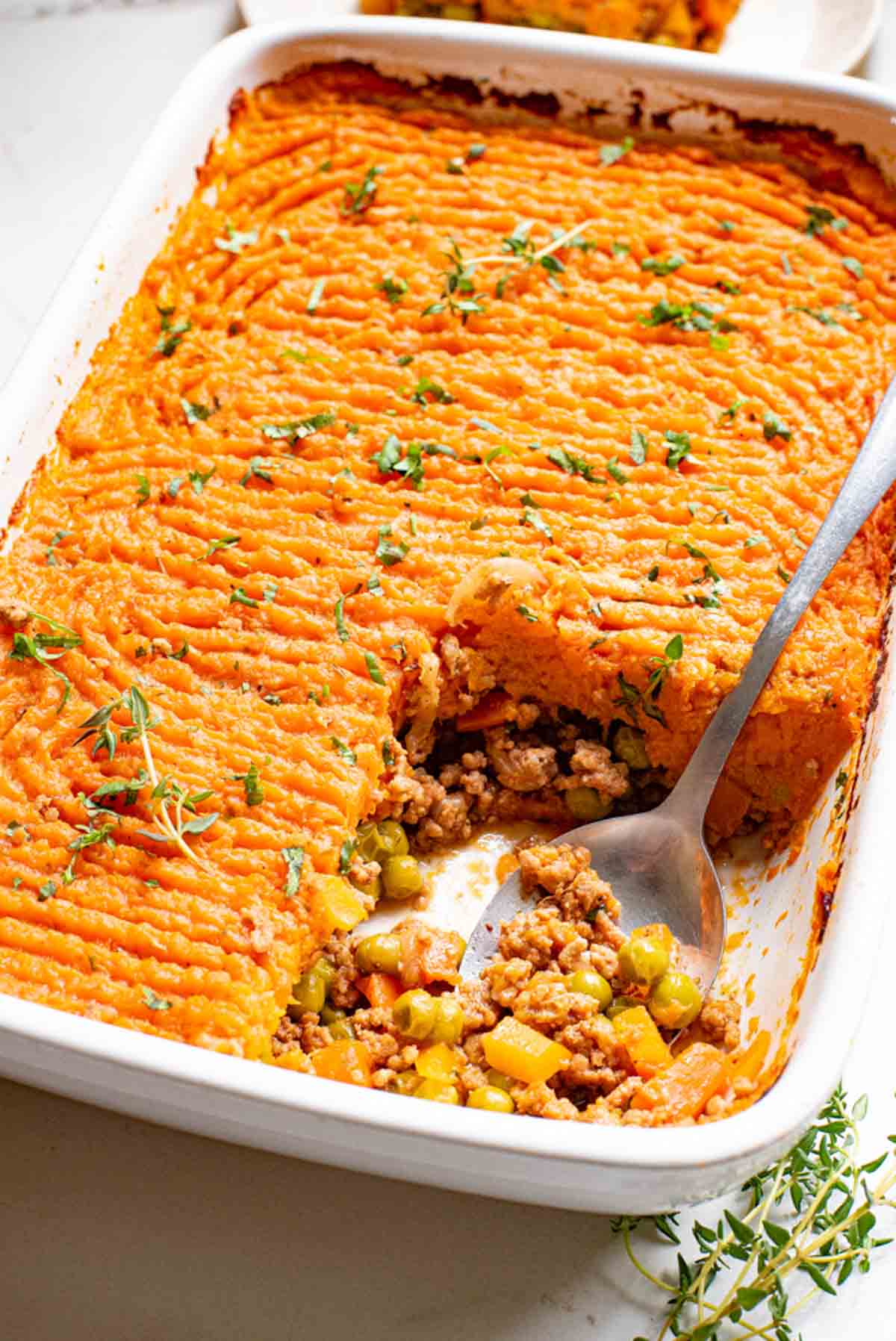 Overhead view of a metal spoon scooping a serving of sweet potato shepherd's pie from a casserole dish.