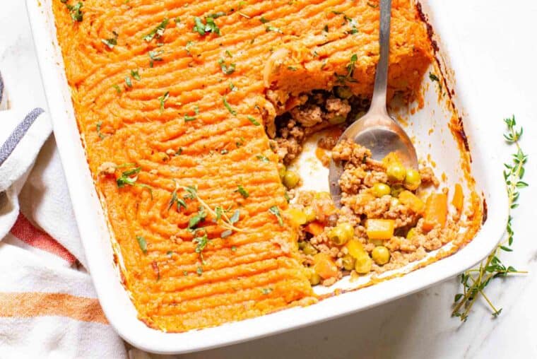 Overhead view of a metal spoon scooping a serving of sweet potato shepherd's pie from a casserole dish.