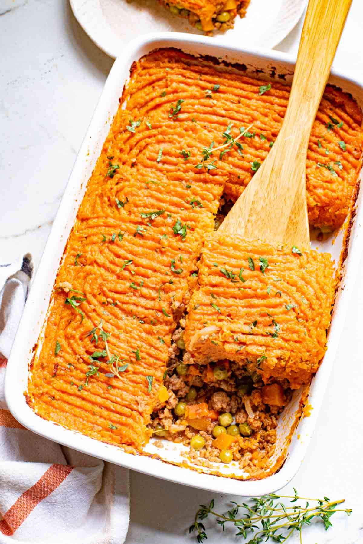 Overhead view of a wooden spoon lifting a serving of sweet potato shepherd's pie from a casserole dish.