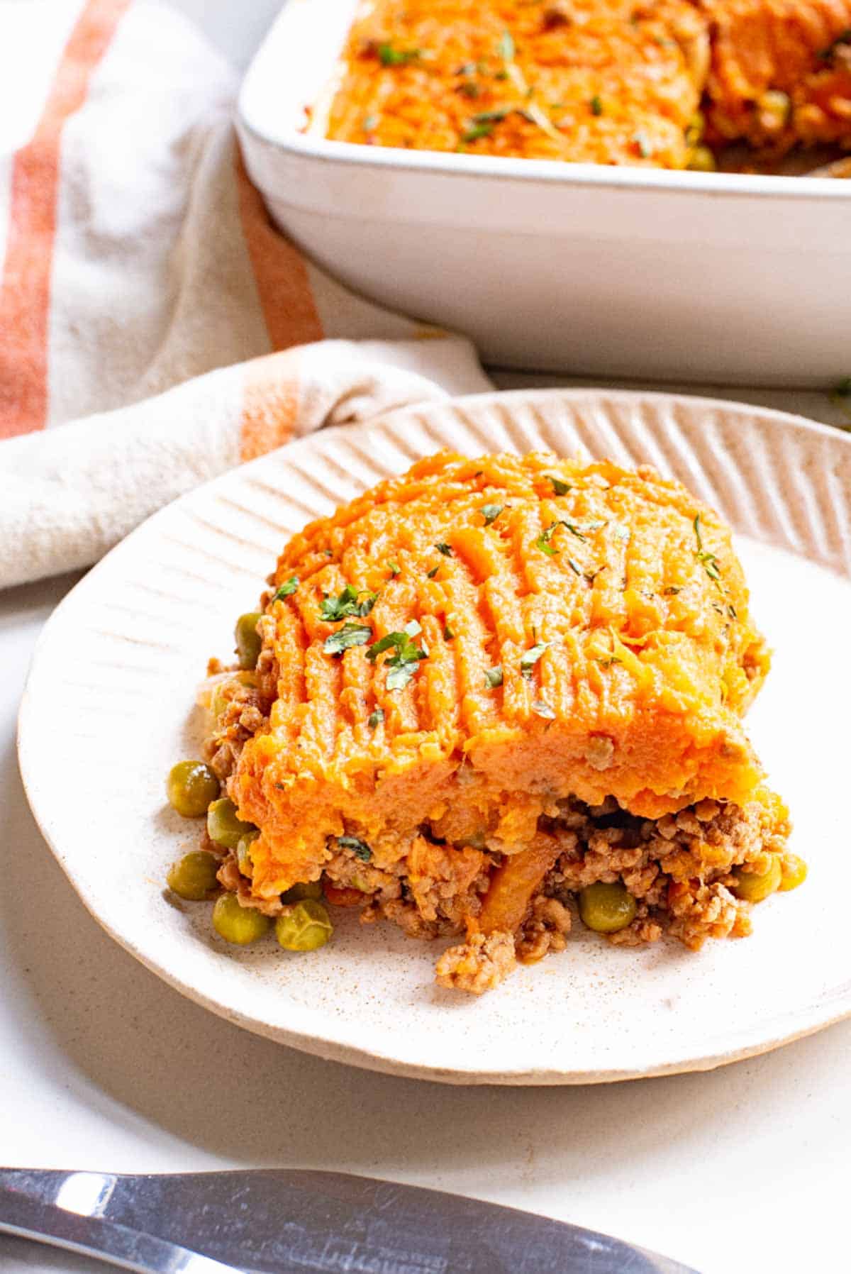 A serving of sweet potato shepherd's pie on a plate, next to a casserole dish.