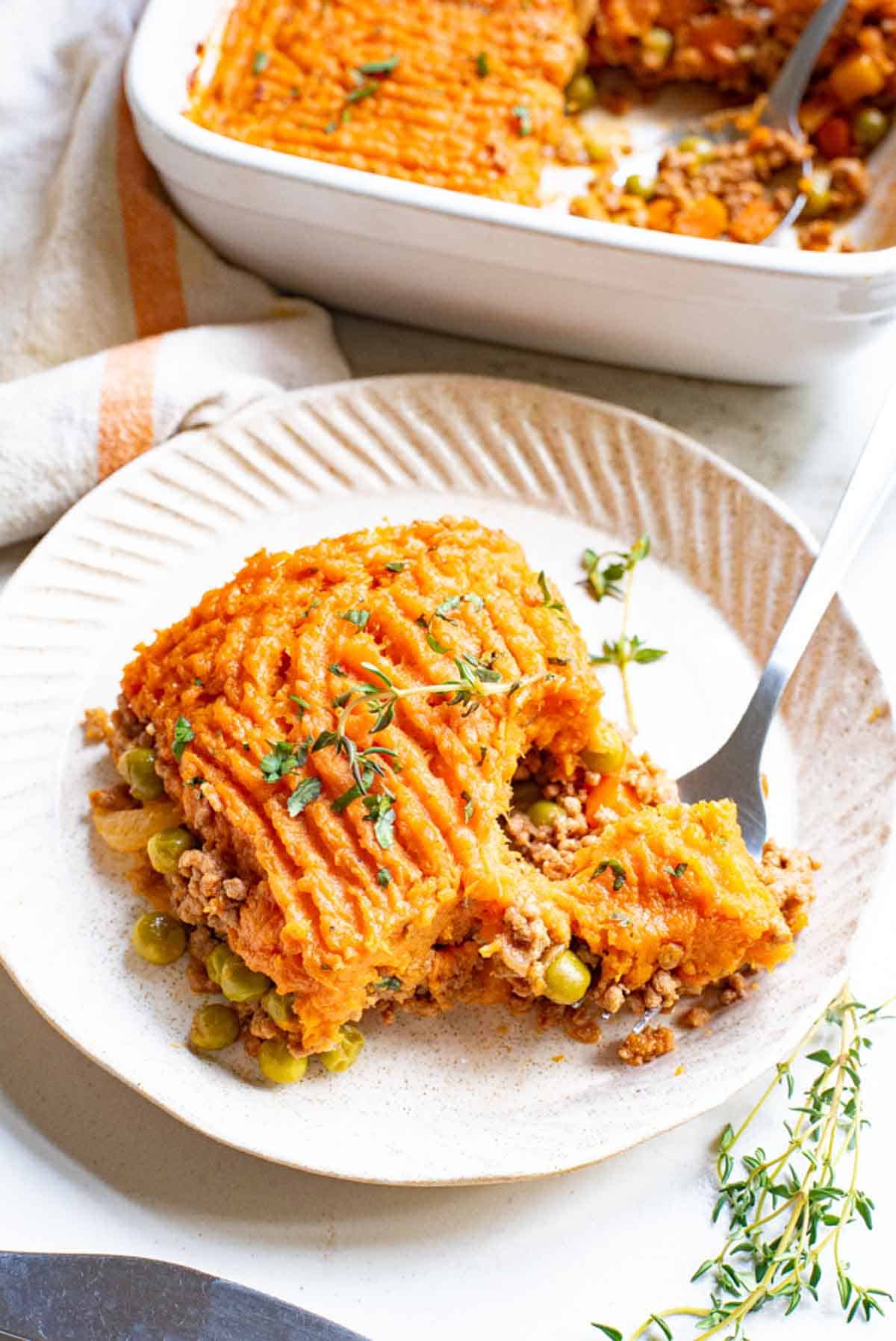 A serving of sweet potato shepherd's pie on a plate, next to a casserole dish.