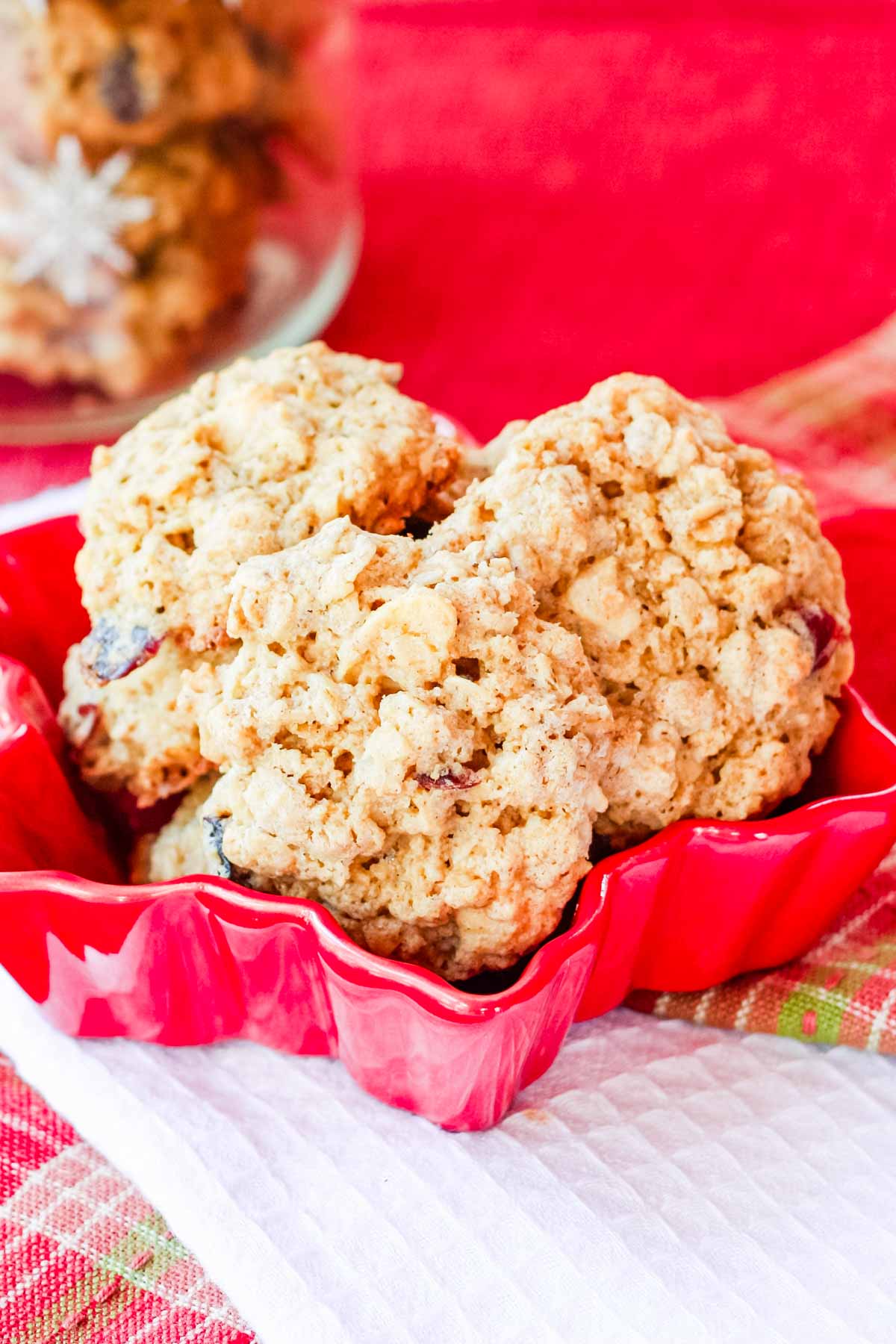 Gluten Free Oatmeal Cookies tied in a red snowflake-shaped dish on top of stacked white and plaid cloth napkins.