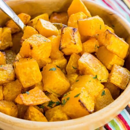 A spoon in a bowl of roasted air fryer butternut squash cubes on top of a striped napkin.