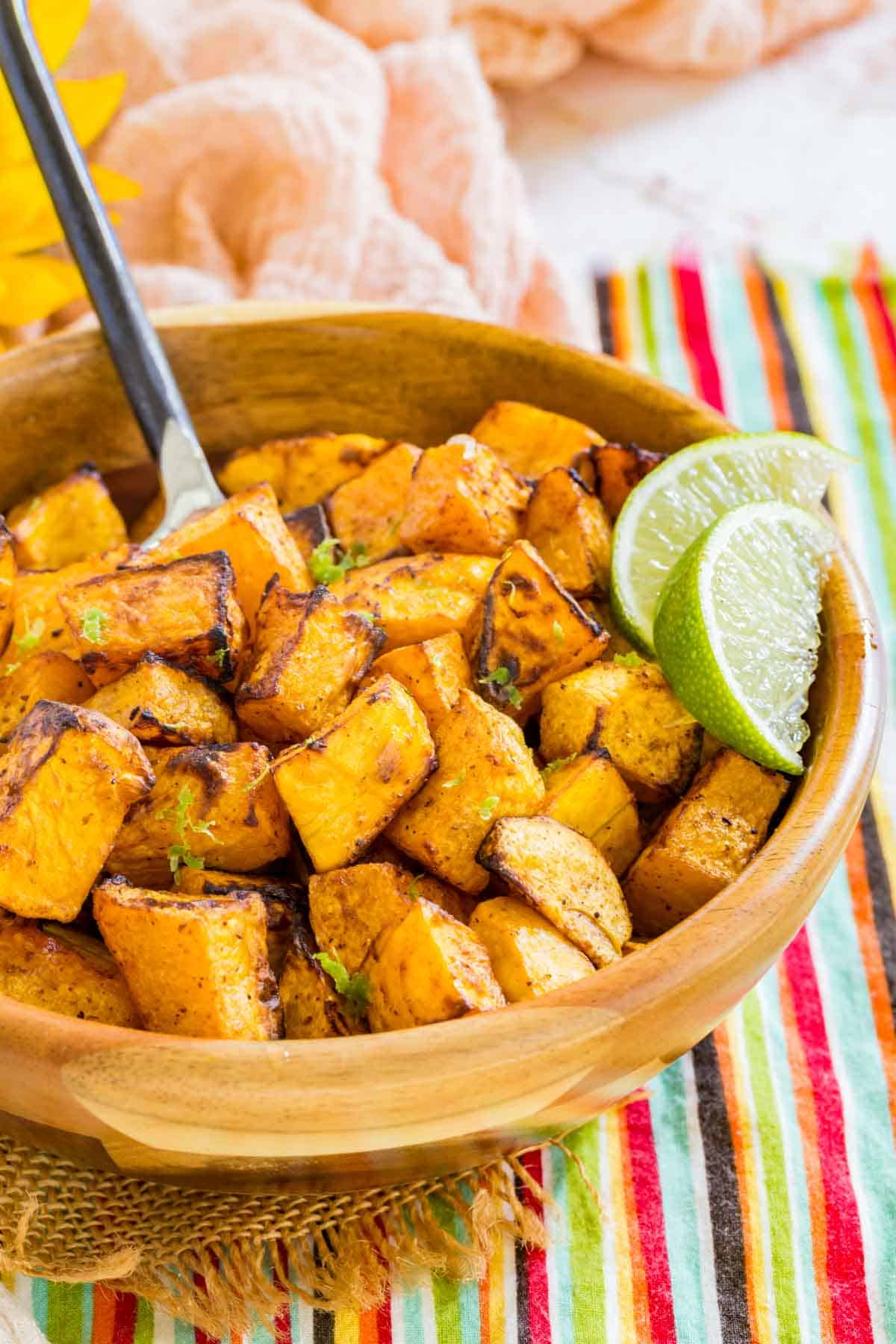 Cubes of roasted butternut squash in a wooden bowl garnished with lime zest and lime wedges.