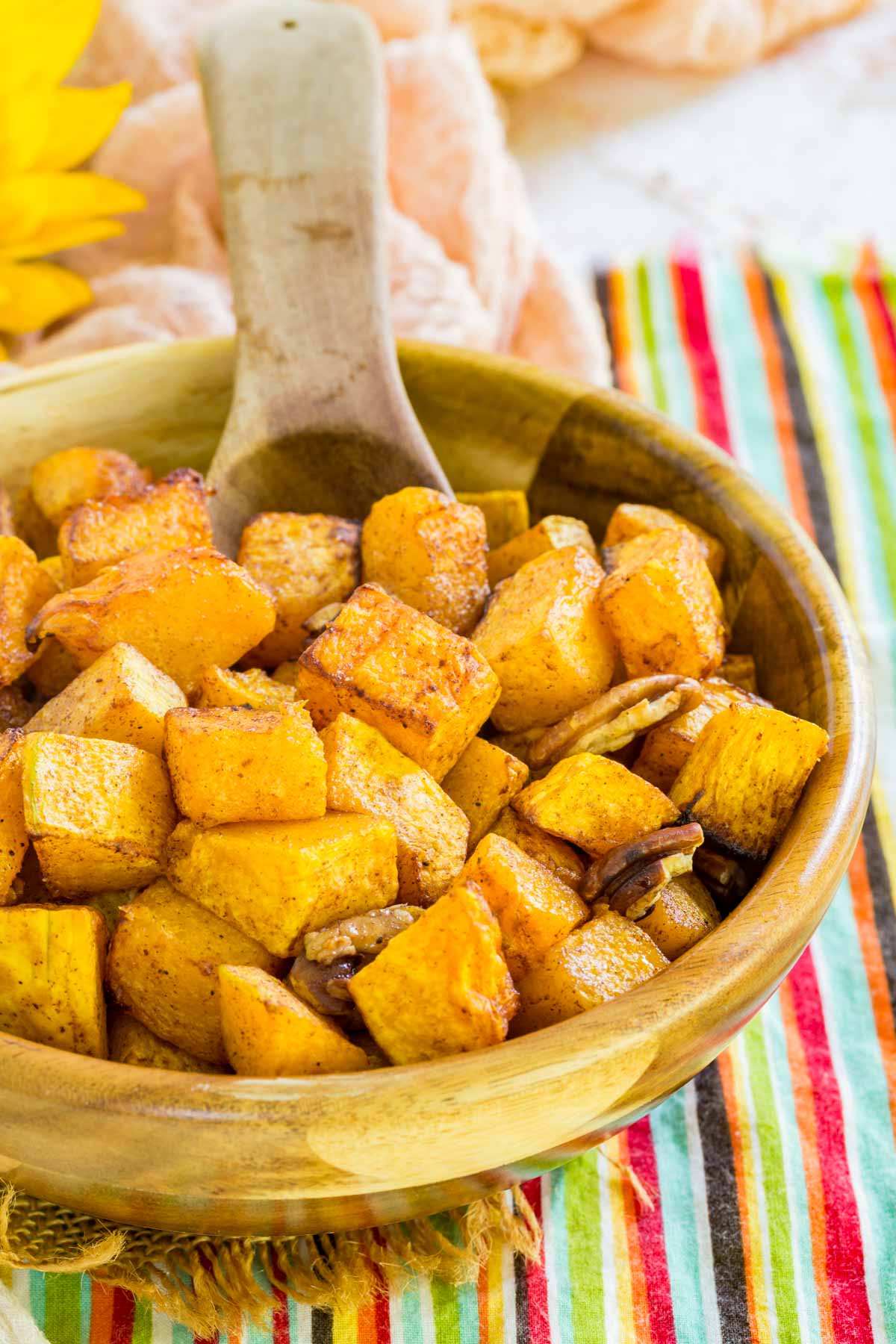 A wooden spoon in a bowl of roasted butternut squash with pecans.