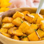 A spoon in a wooden bowl of roasted butternut squash cubes garnished with parsley and pepper with text overlay that says "Air Fryer Butternut Squash".