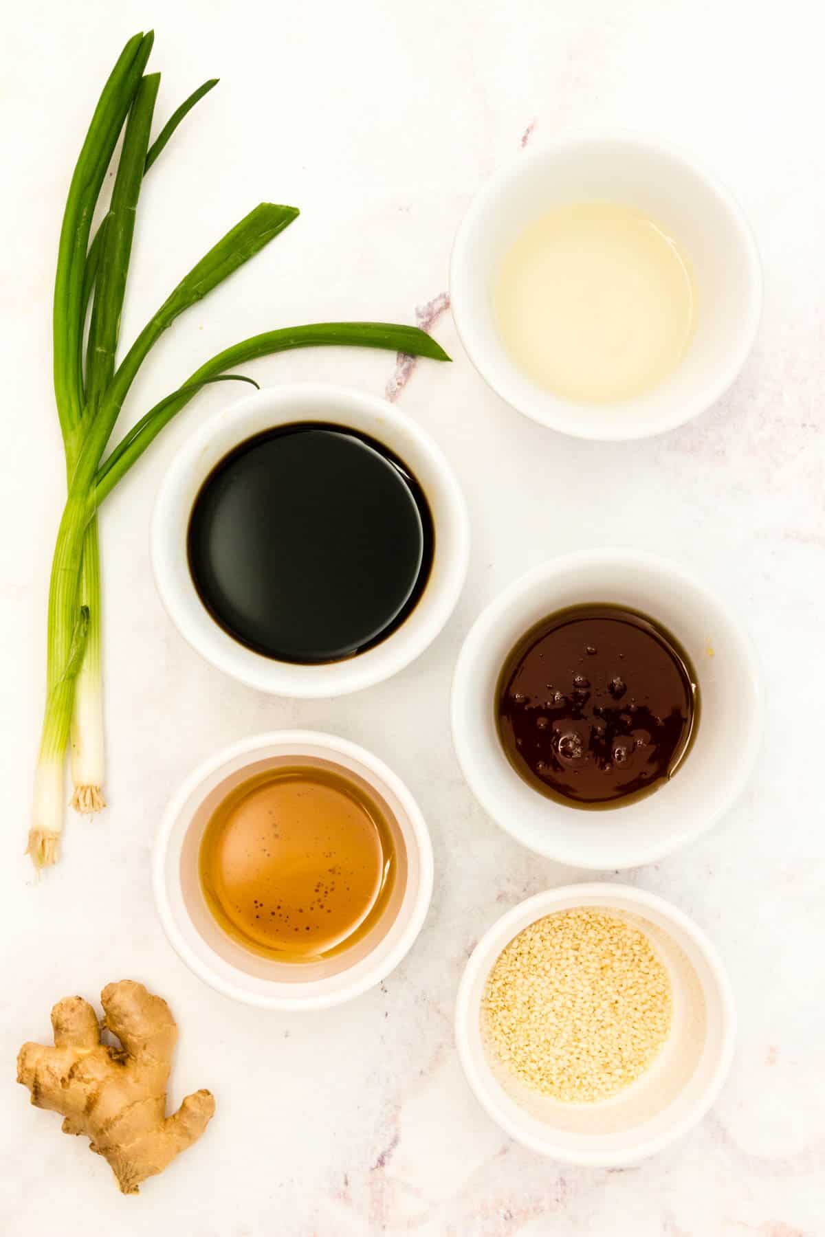 Ingredients to make a sesame and soy sauce glaze in bowls on a marble countertop.