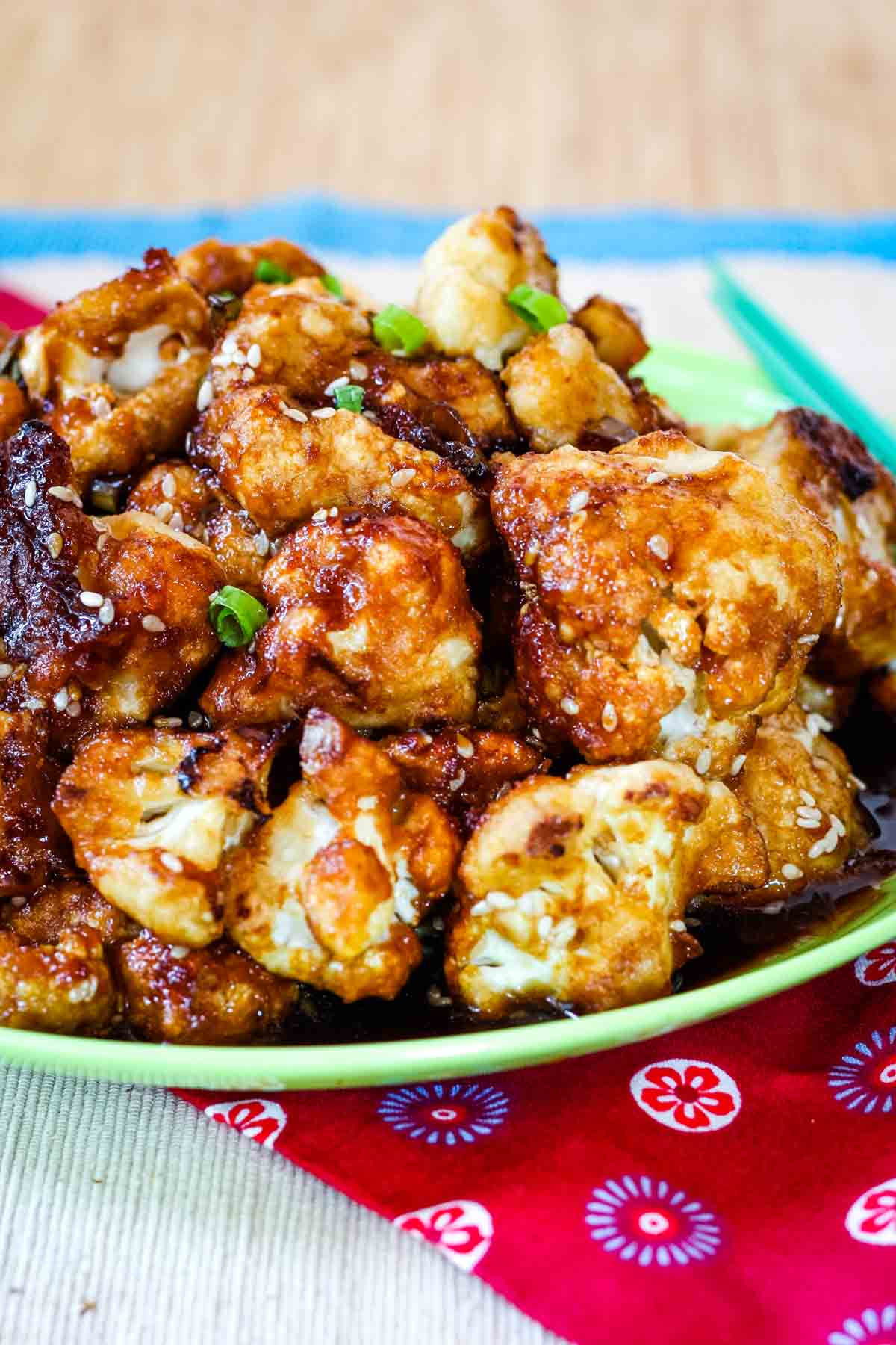 Looking from the side at a pile of cauliflower wings with a dark brown glaze and sesame seeds on a plate.