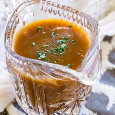 Gluten-free brown gravy in a glass gravy boat, garnished with fresh parsley.