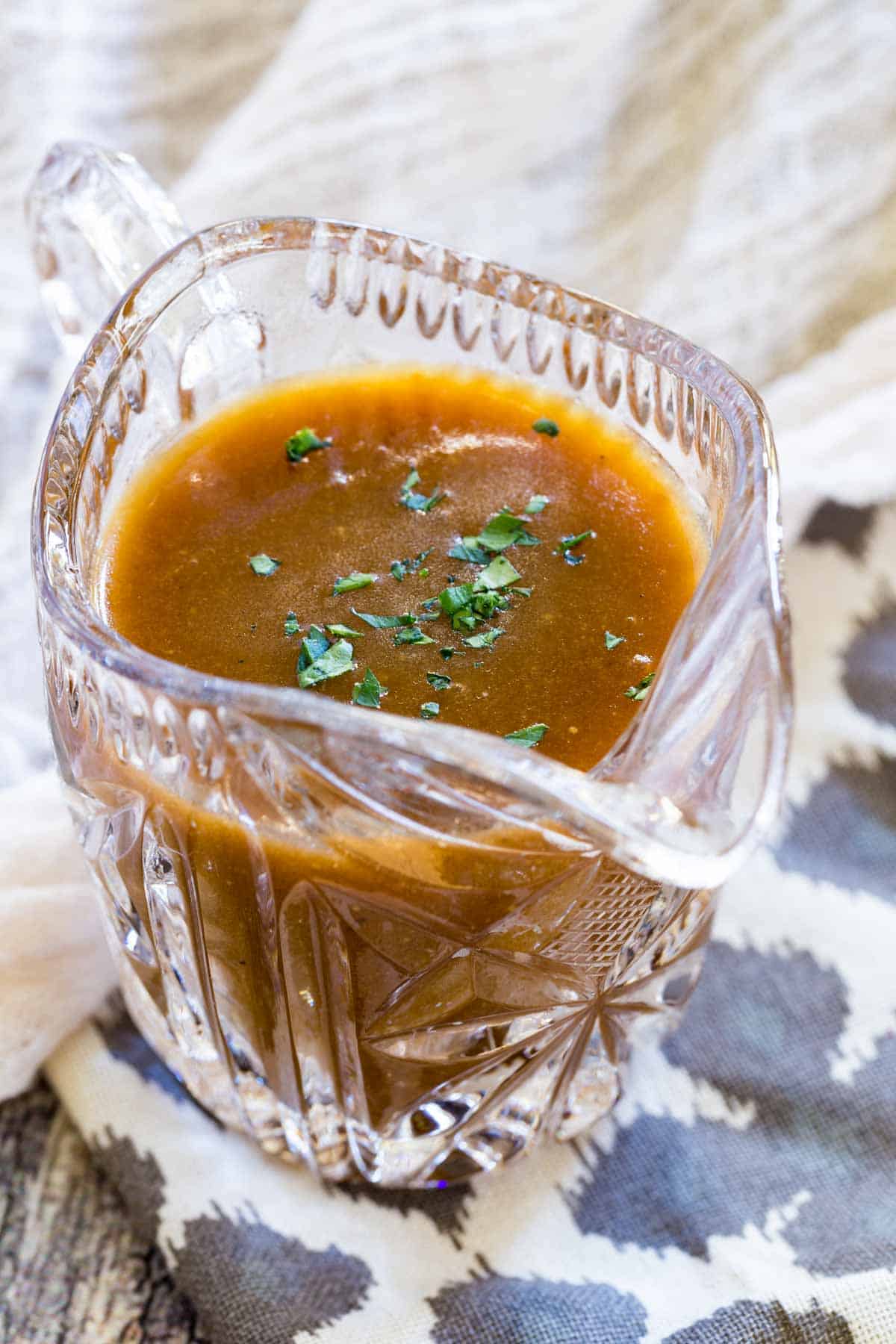 Gluten-free brown gravy in a glass gravy boat, garnished with fresh parsley.