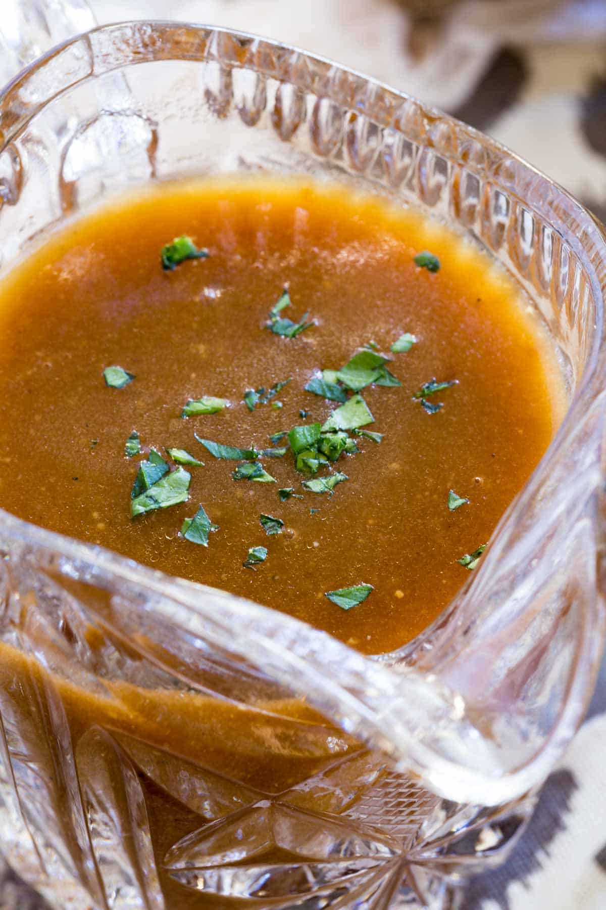 Close up of gluten-free brown gravy in a glass gravy boat, garnished with fresh parsley.