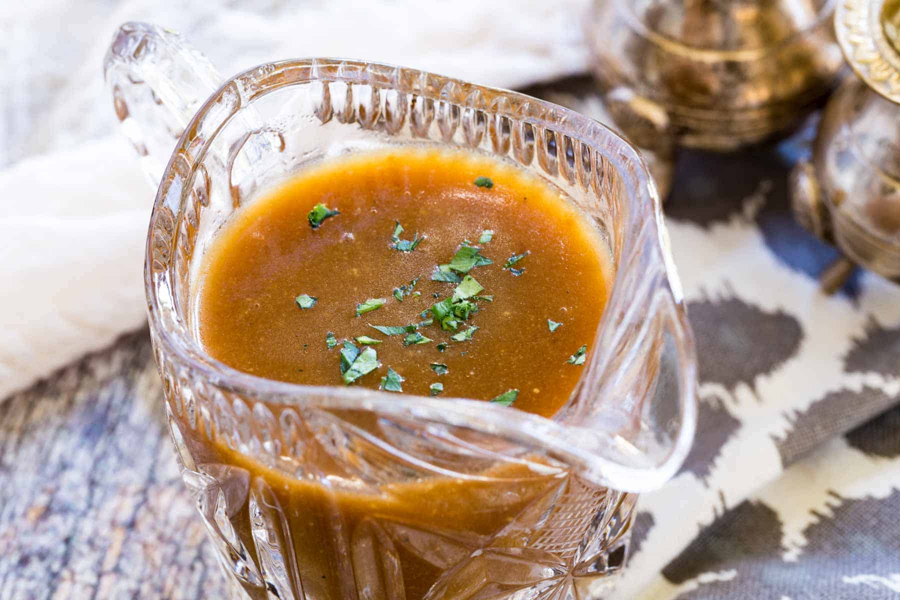 Gluten-free brown gravy in a glass gravy boat, garnished with fresh parsley.