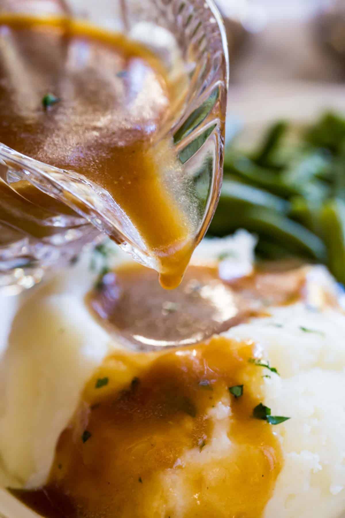 Close up of gluten-free brown gravy being poured over a pile of mashed potatoes on a plate next to green beans.