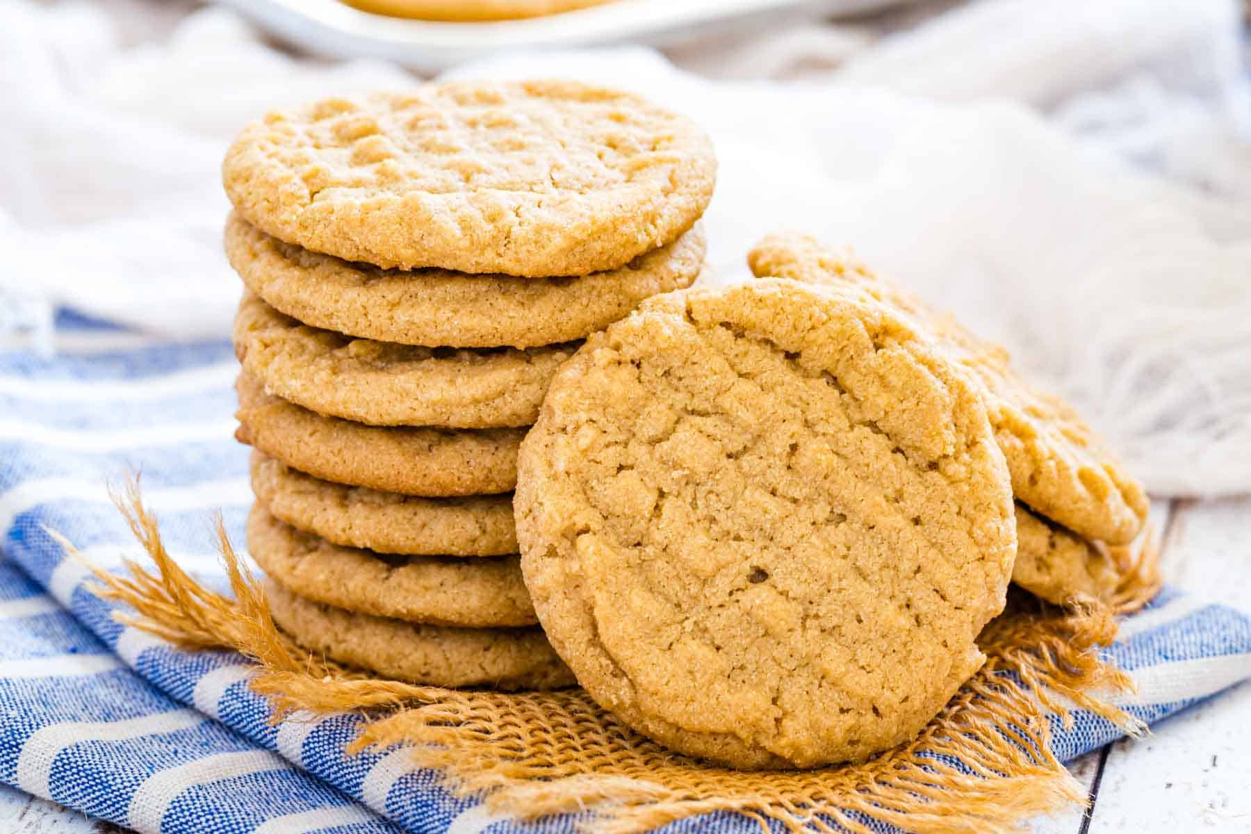 A gluten-free peanut butter cookie leaning against a stack of peanut butter cookies on a blue dishcloth.