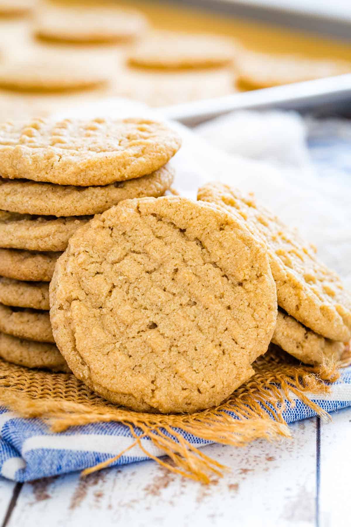 A gluten-free peanut butter cookie leaning against a stack of peanut butter cookies on a blue dishcloth.