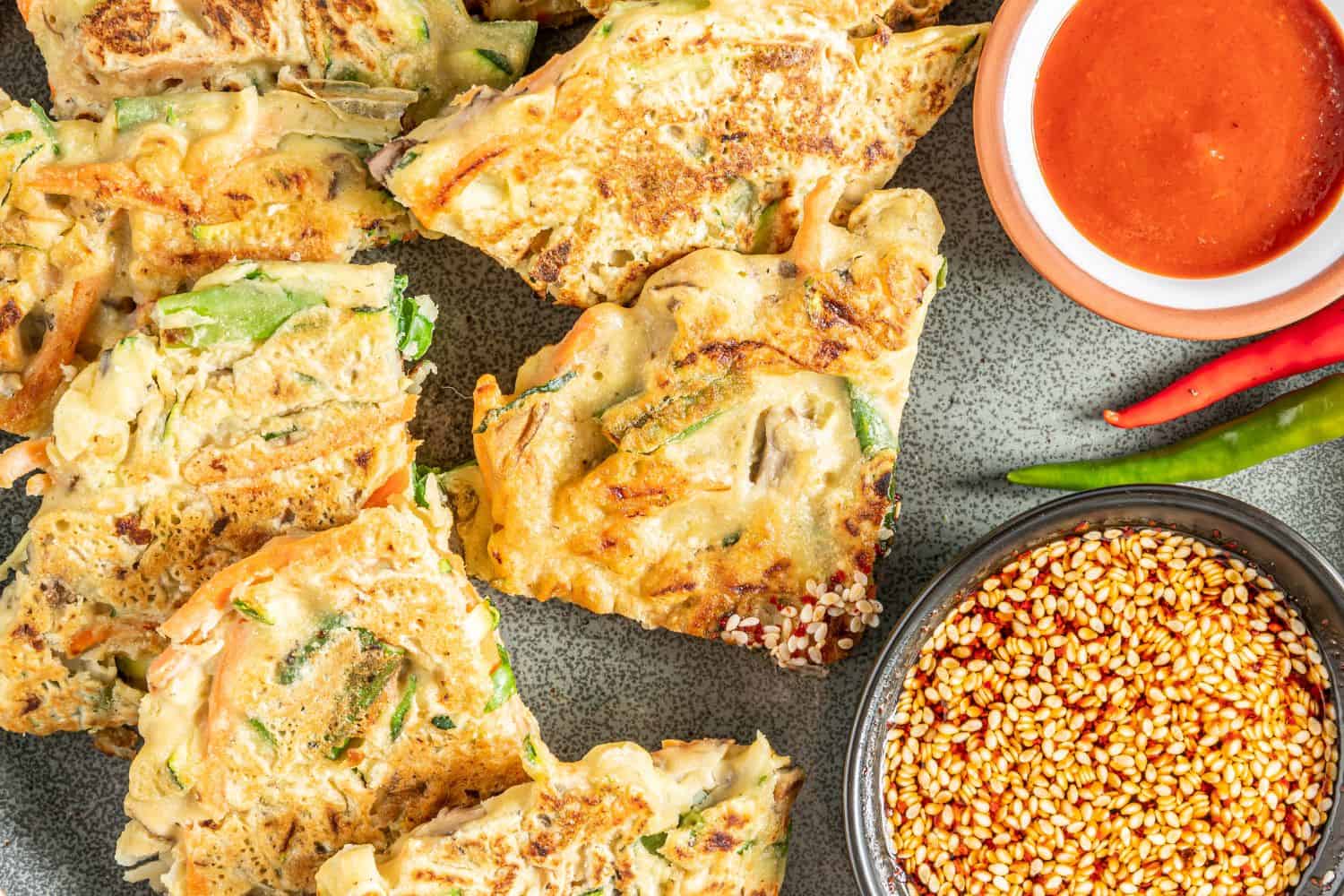 Vegetable pancake wedges on a platter with bowls of dipping sauces.