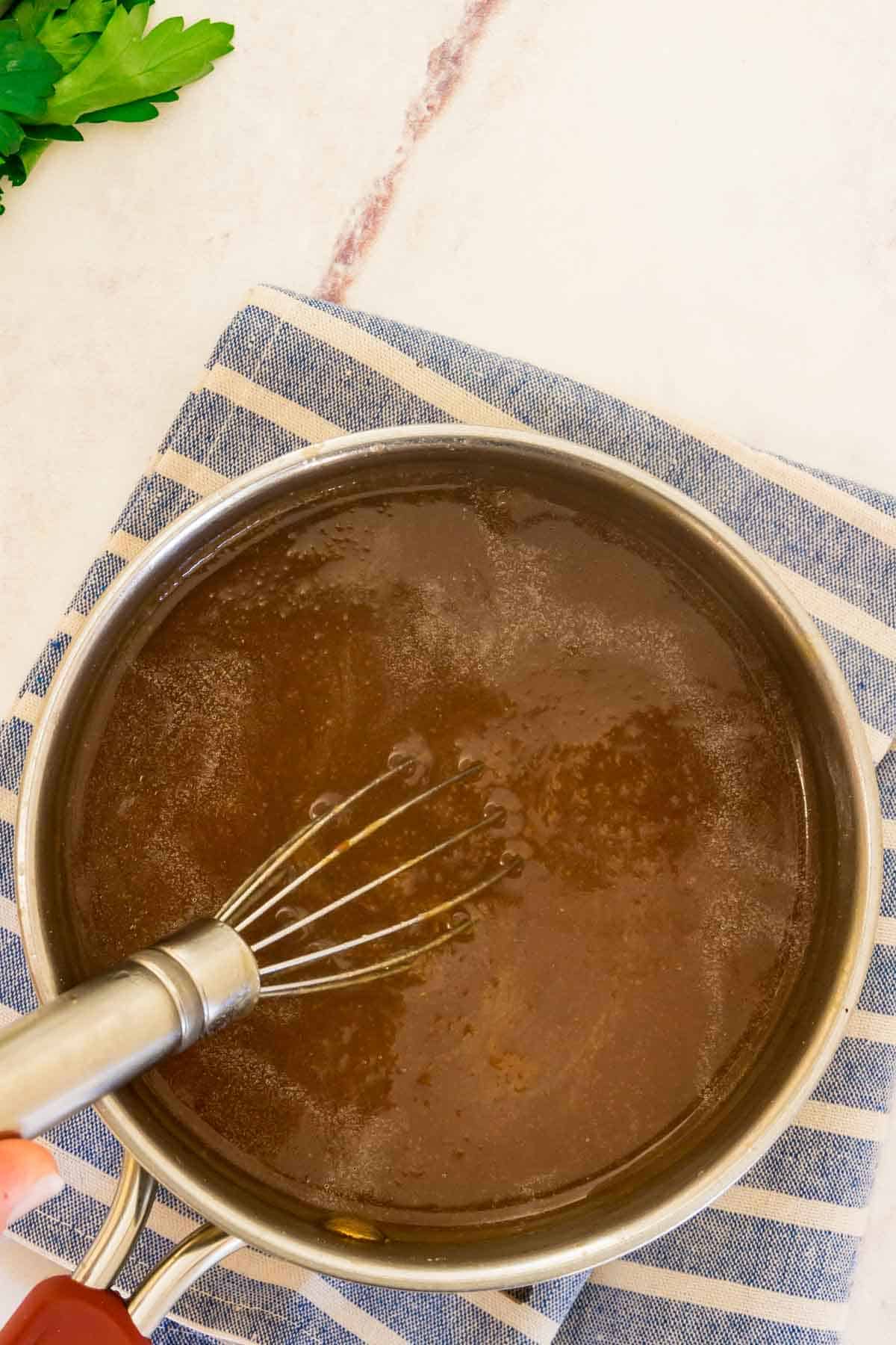 Gluten-free brown gravy simmering in a saucepan with a whisk.