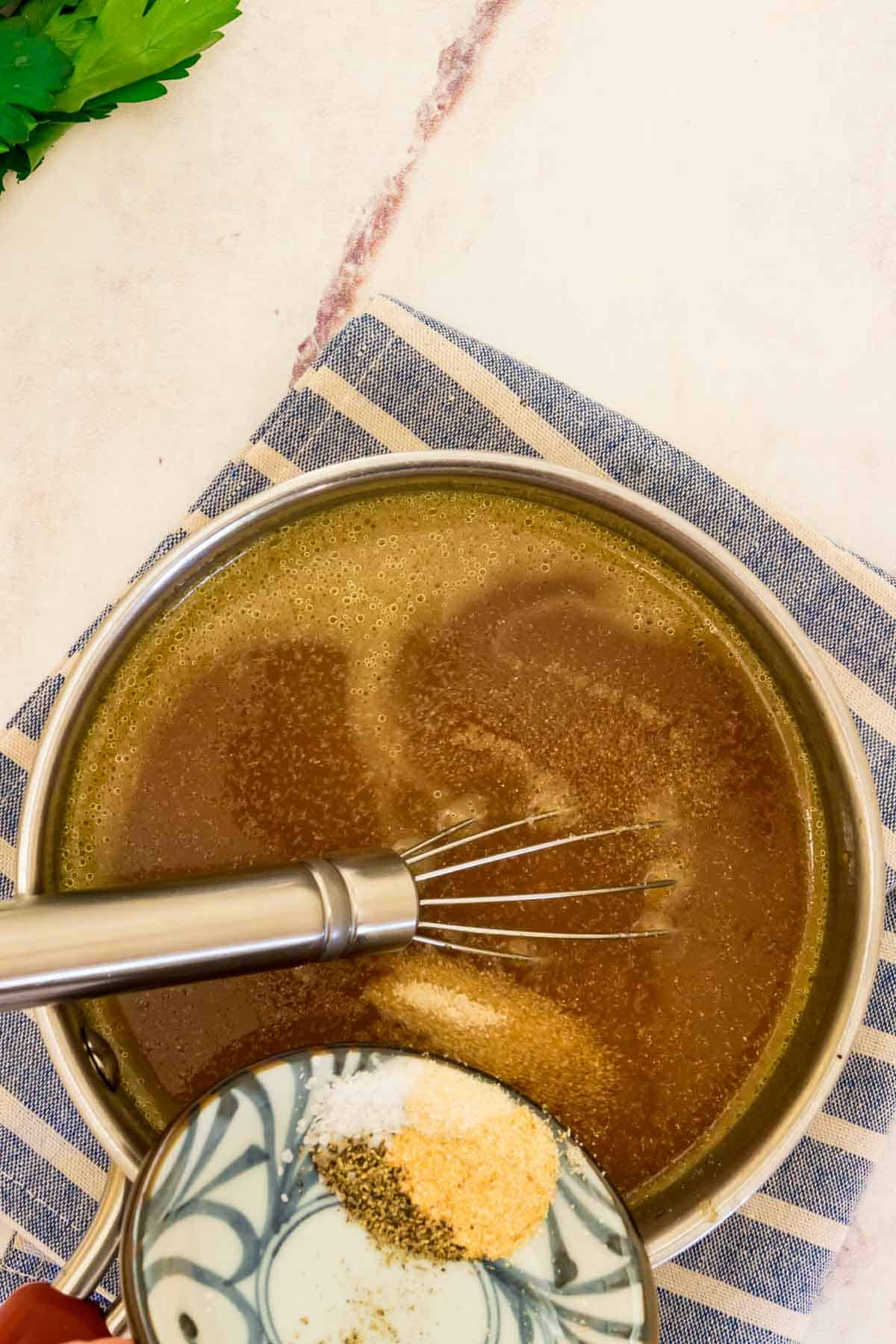 Seasonings are added into a saucepan with brown gravy.