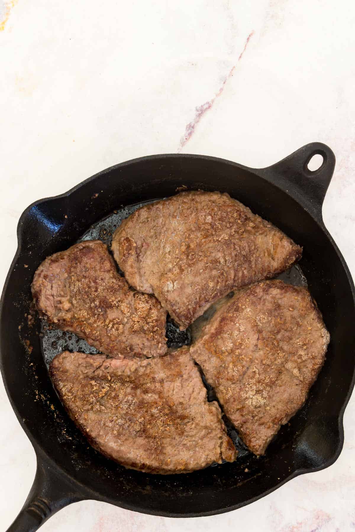 Four seared cube steaks in a cast iron skillet.