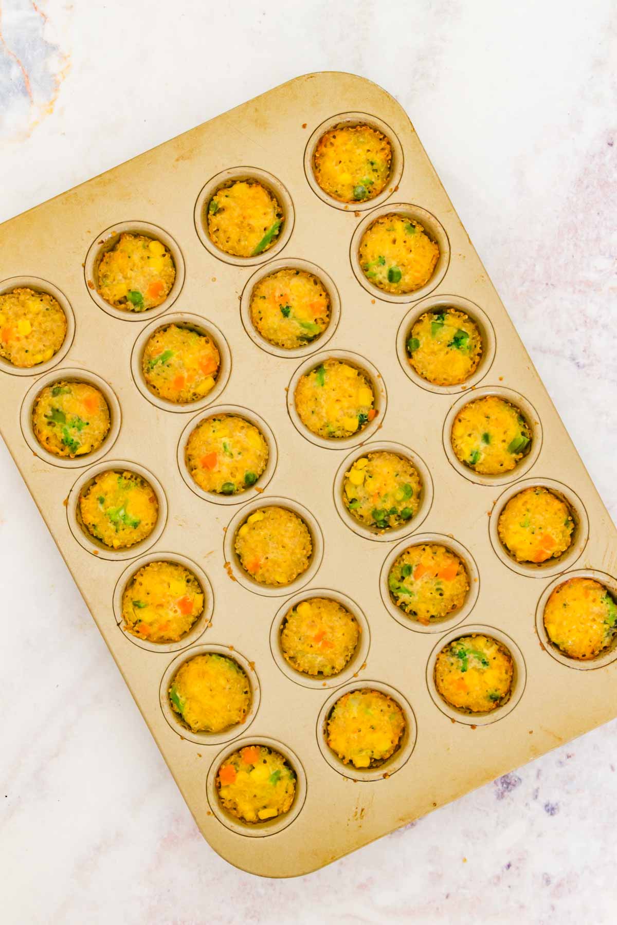 Fully baked cheesy quinoa bites in a mini muffin pan.
