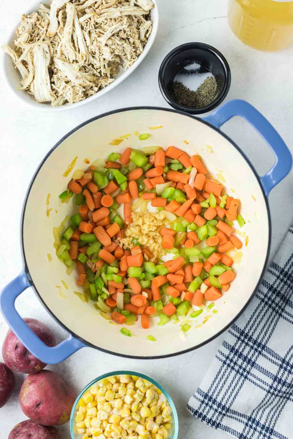 Carrots, celery, onions, and garlic sauteing in a large pot with oil, surrounded by chicken soup ingredients.