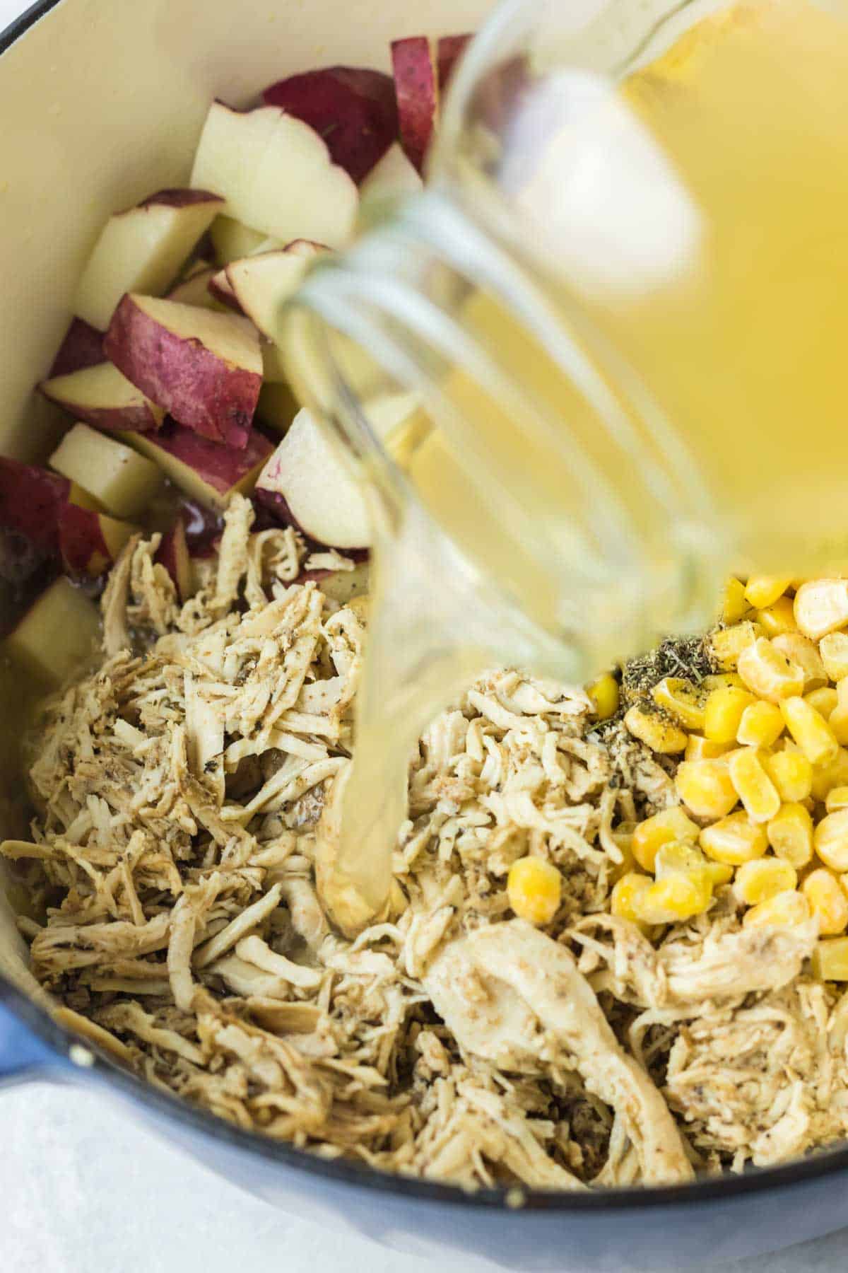 Chicken stock is poured from a glass mason jar into a pot of chicken soup ingredients.