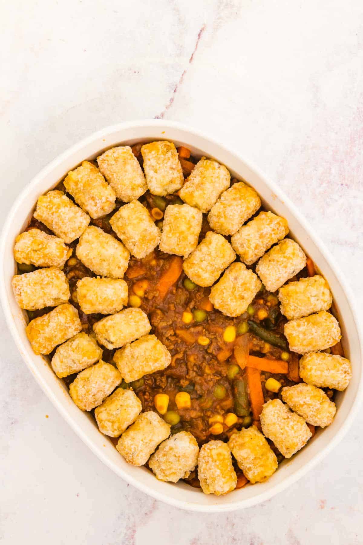Tater tots are added over top the shepherd's pie filling in an oval casserole dish.