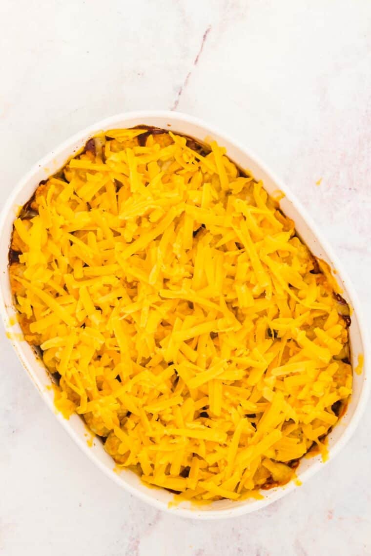 Shredded cheese layered over baked tater tot shepherd's pie in a casserole dish.