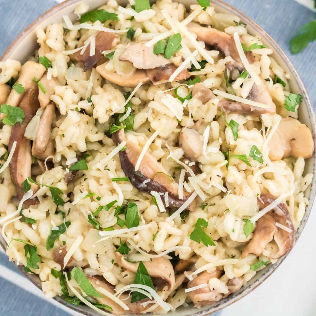 Looking down at a bowl of mushroom risotto sprinkled with minced parsley and shredded parmesan cheese.