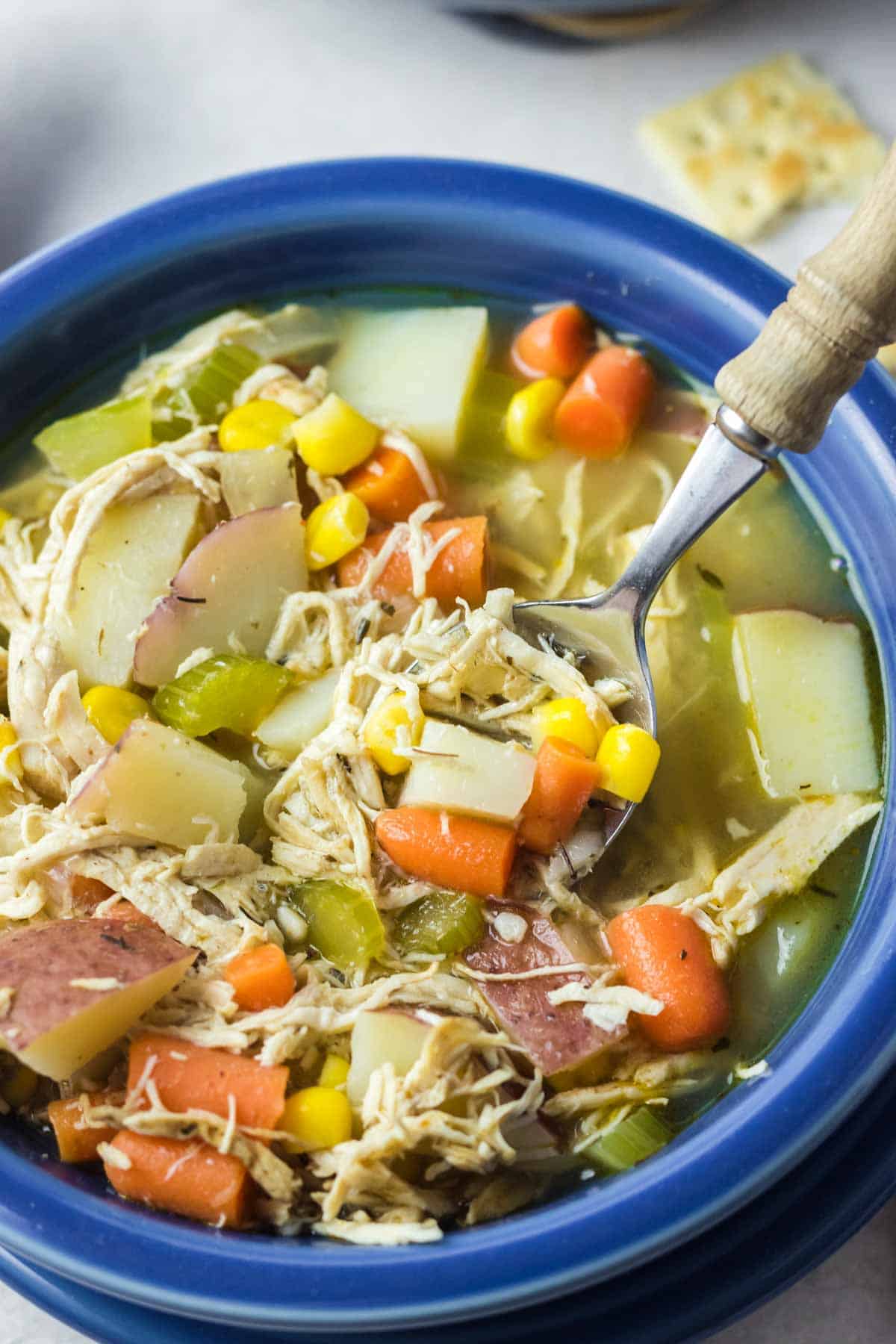 Close-up overhead view of a serving of rotisserie chicken soup in a blue bowl with a spoon.