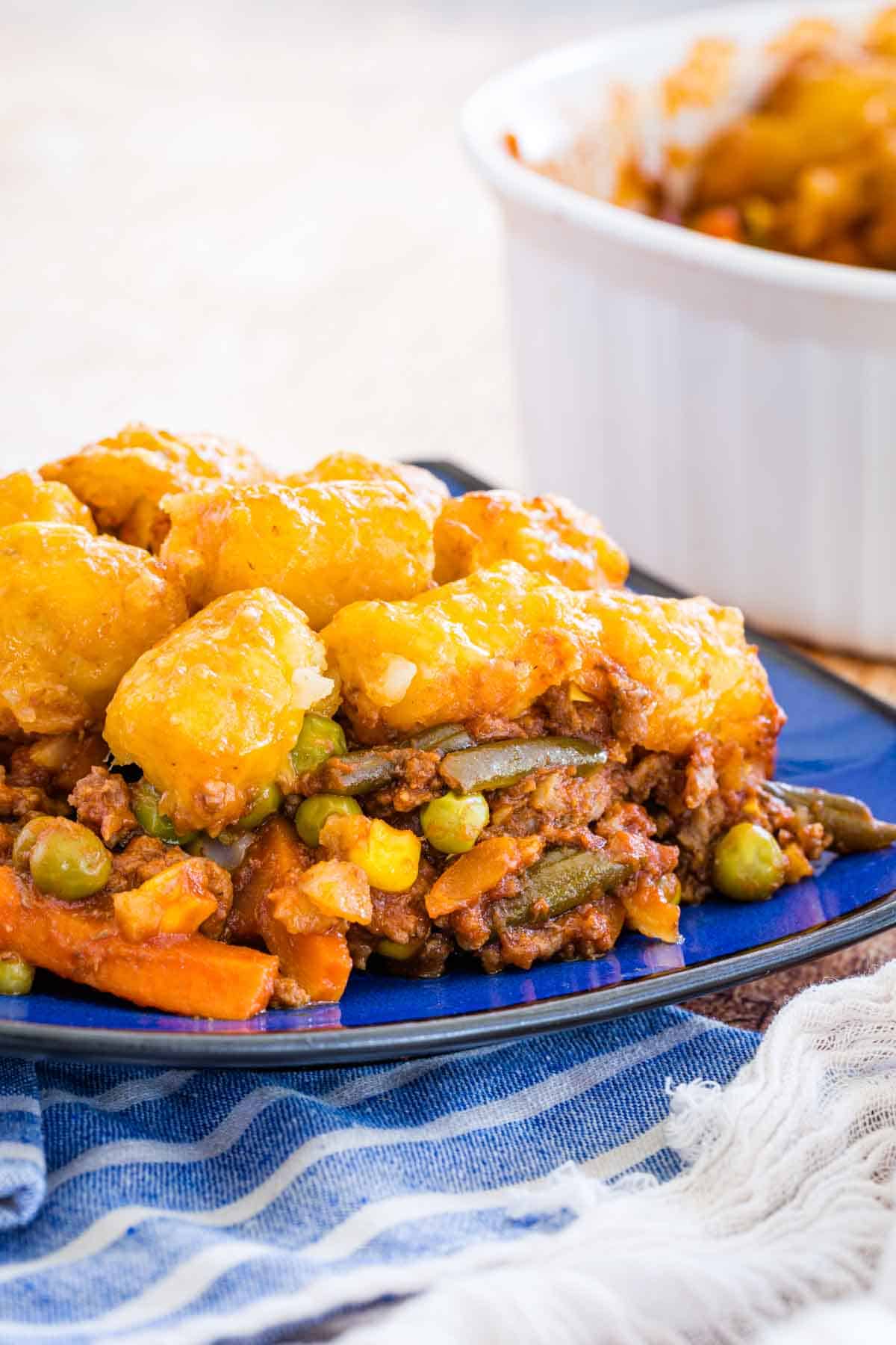 A serving of tater tot shepherd's pie on a blue plate next to a casserole dish.