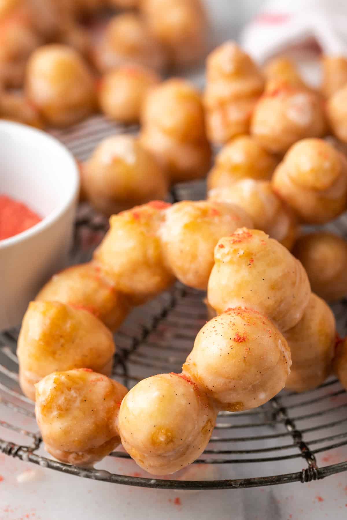 Gluten-free mochi donuts on a wire rack, next to a small bowl of crushed freeze-dried fruit powder.