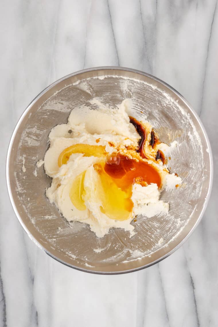 Vanilla and egg whites added to creamed sugar and butter in a metal mixing bowl.