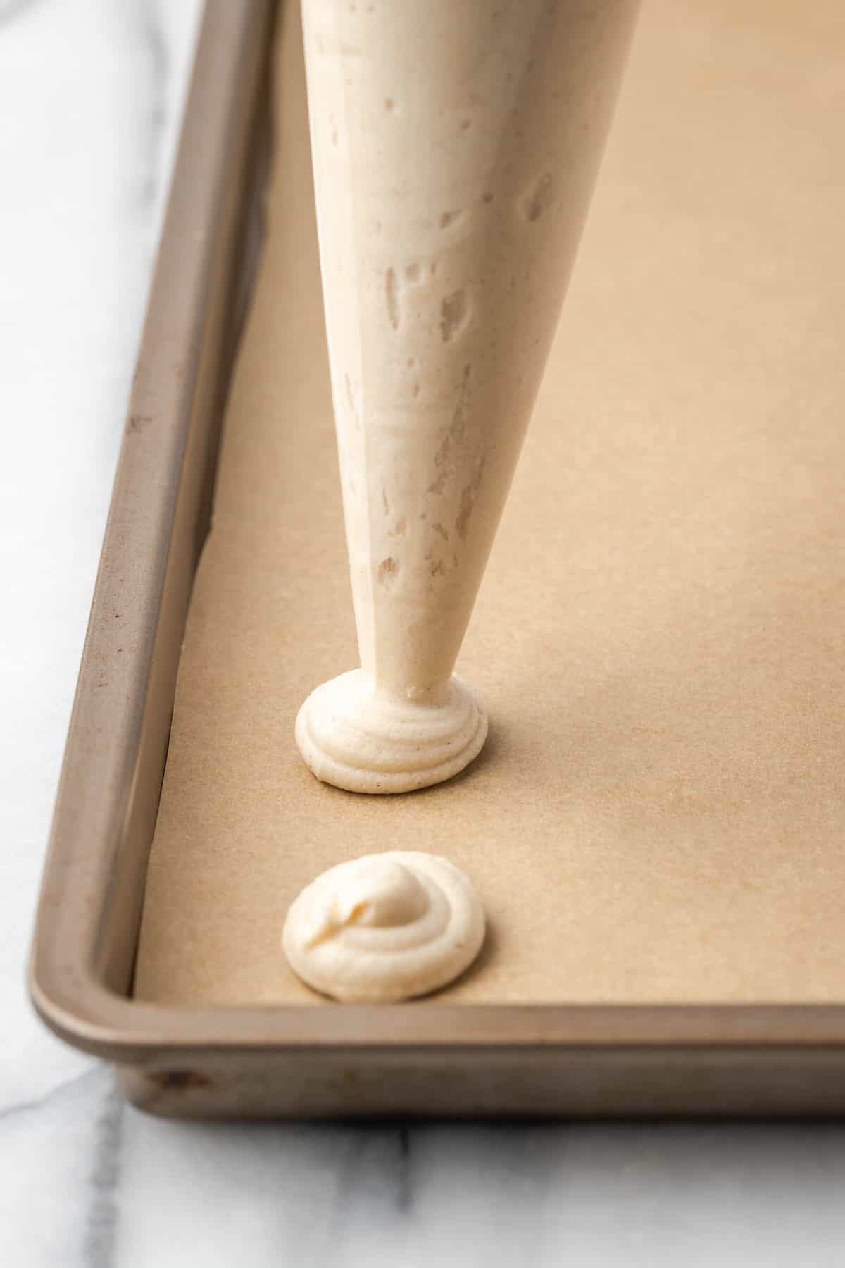 A piping bag pipes swirls of gluten-free wafer batter onto a lined baking sheet.