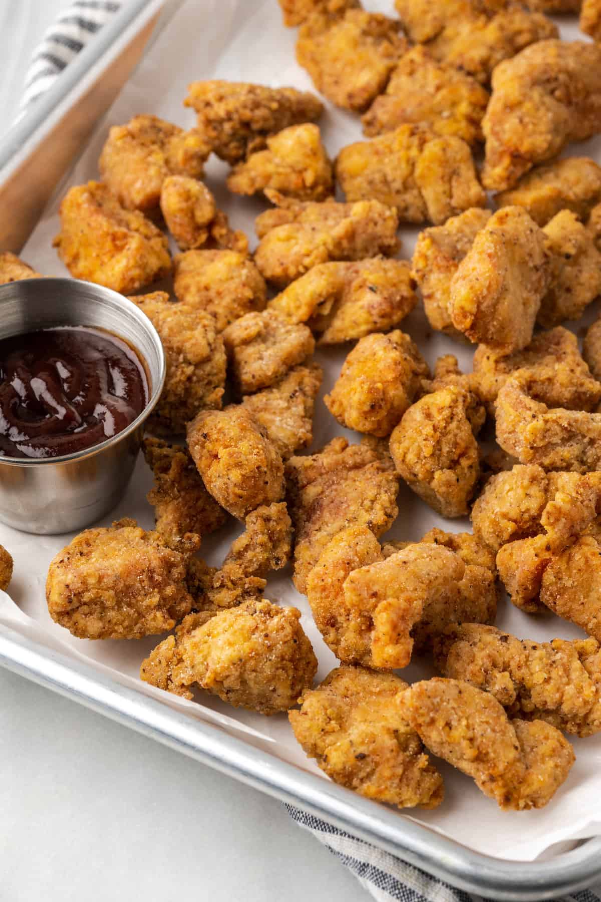 Gluten-free KFC popcorn chicken in a metal platter next to a ramekin of BBQ sauce.