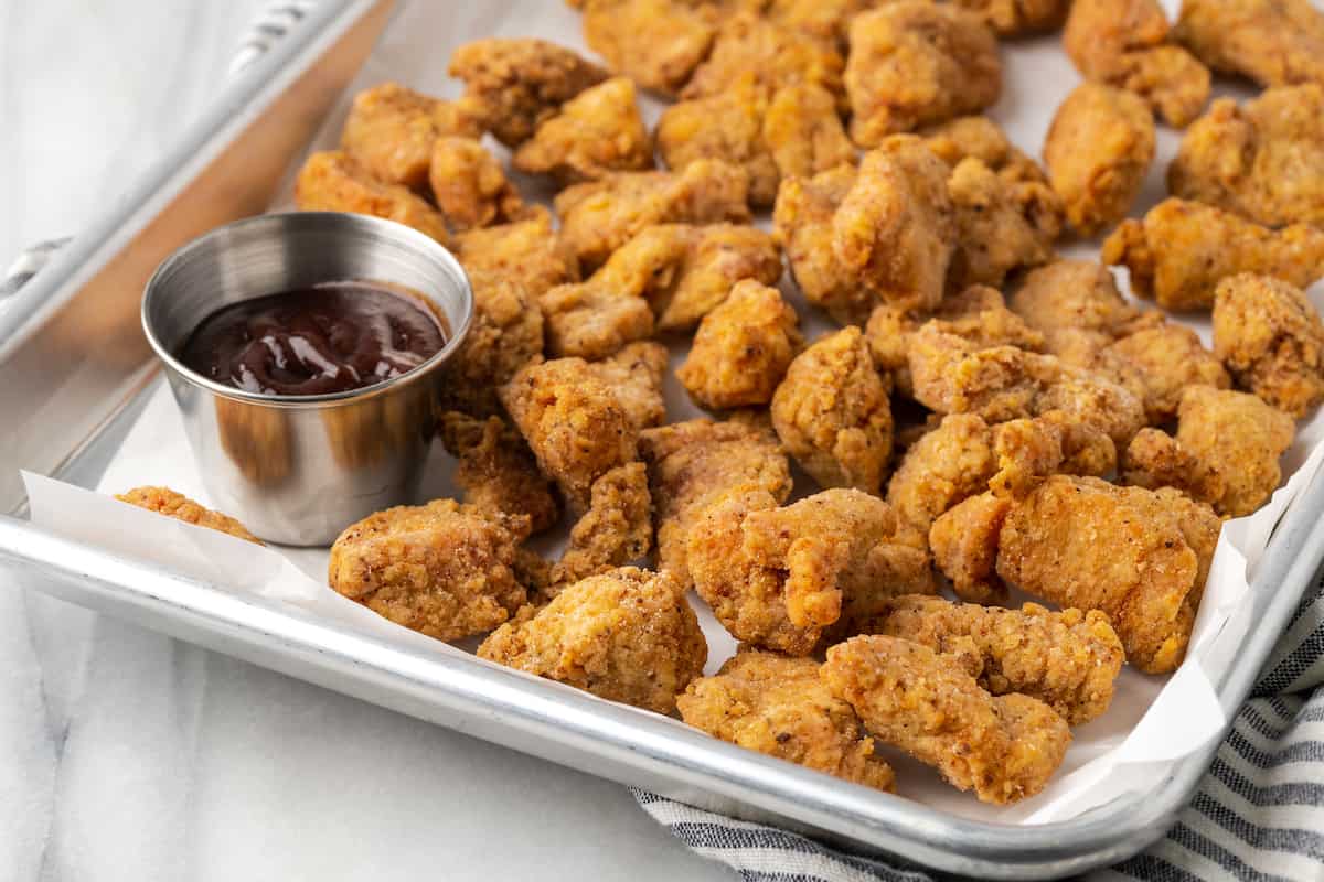 Gluten-free KFC popcorn chicken in a metal platter next to a ramekin of BBQ sauce.