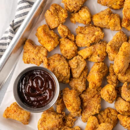 Overhead view of gluten-free KFC popcorn chicken in a metal platter next to a ramekin of BBQ sauce.