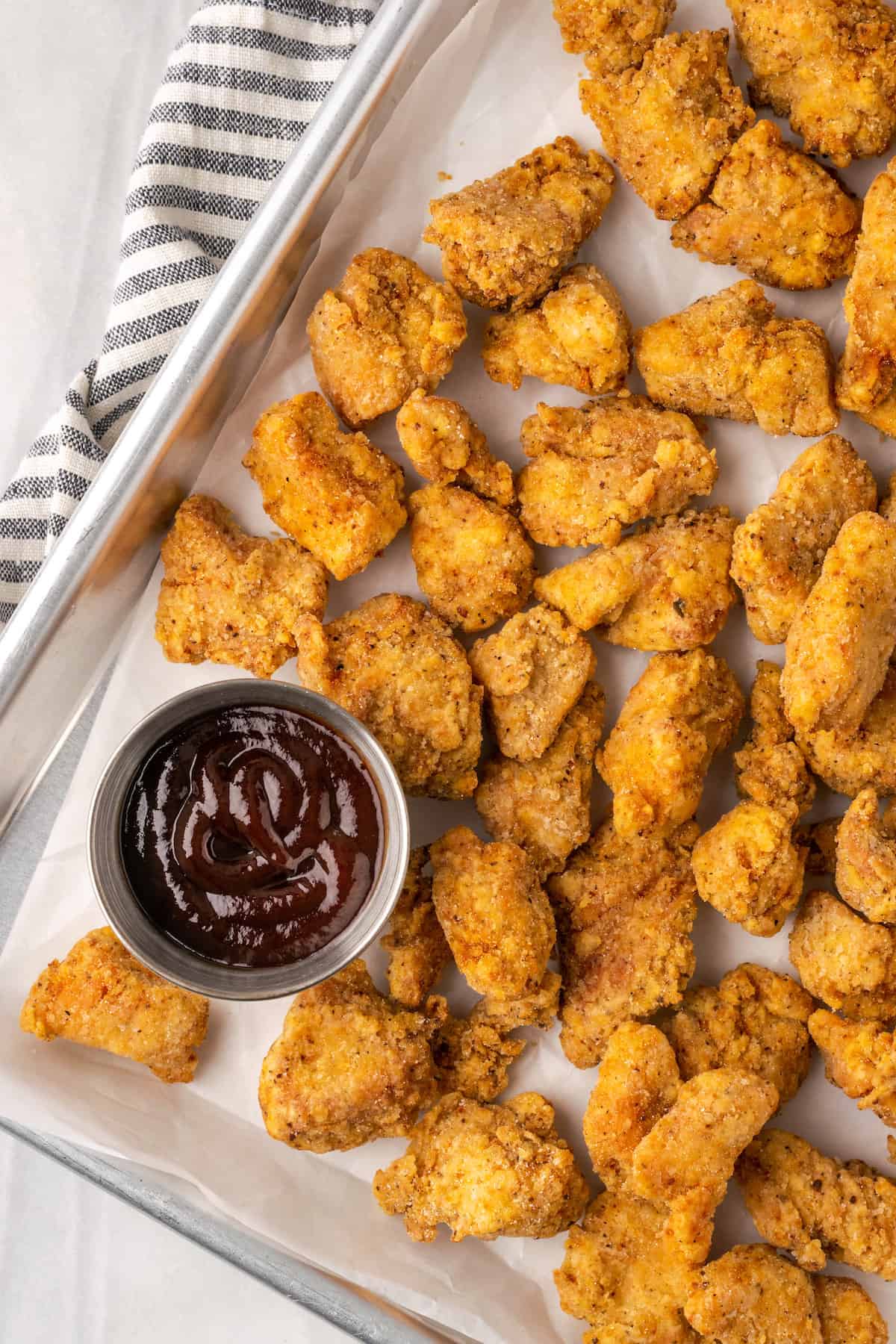 Overhead view of gluten-free KFC popcorn chicken in a metal platter next to a ramekin of BBQ sauce.