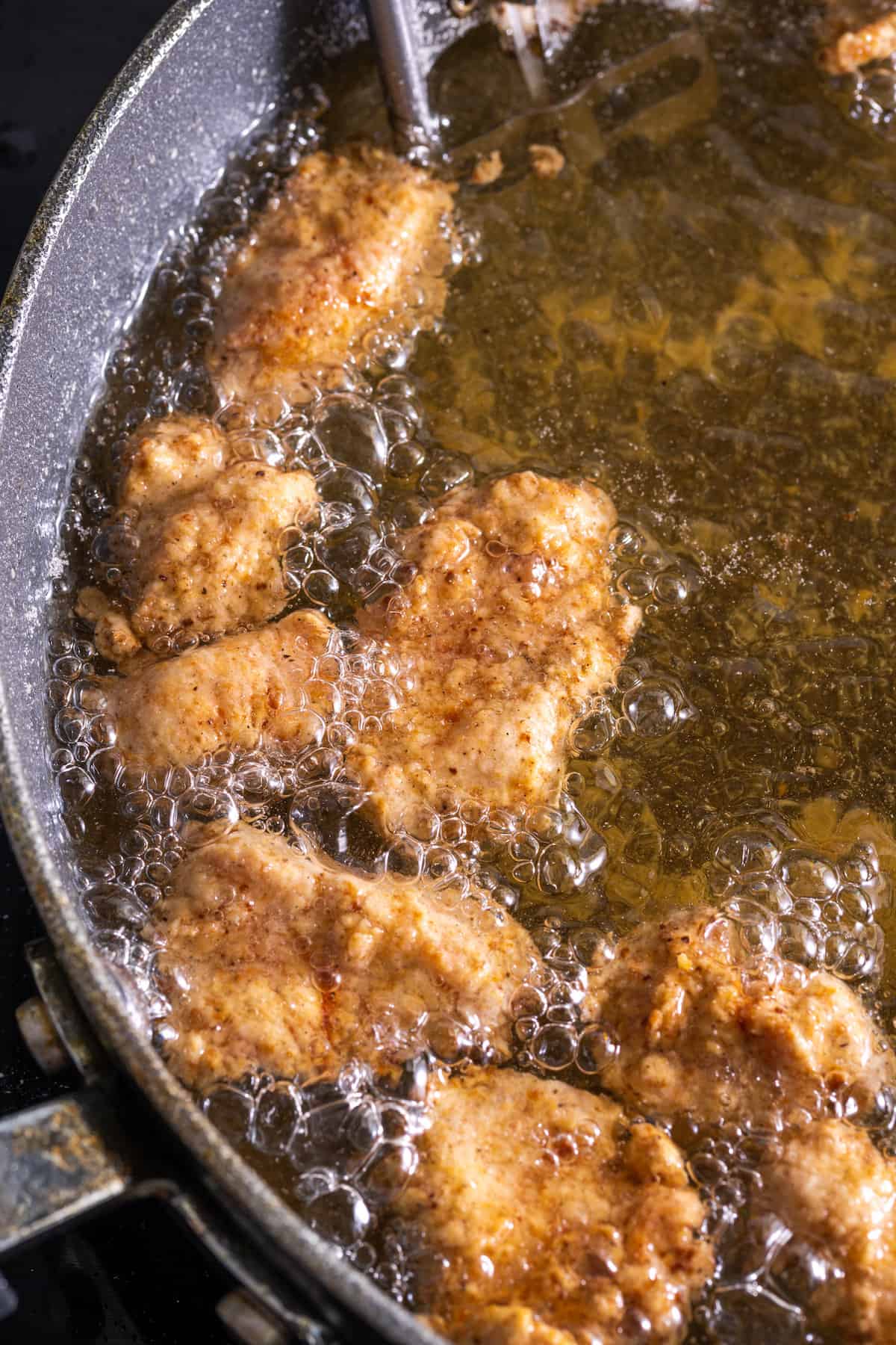 Gluten-free popcorn chicken deep frying in a skillet with oil.
