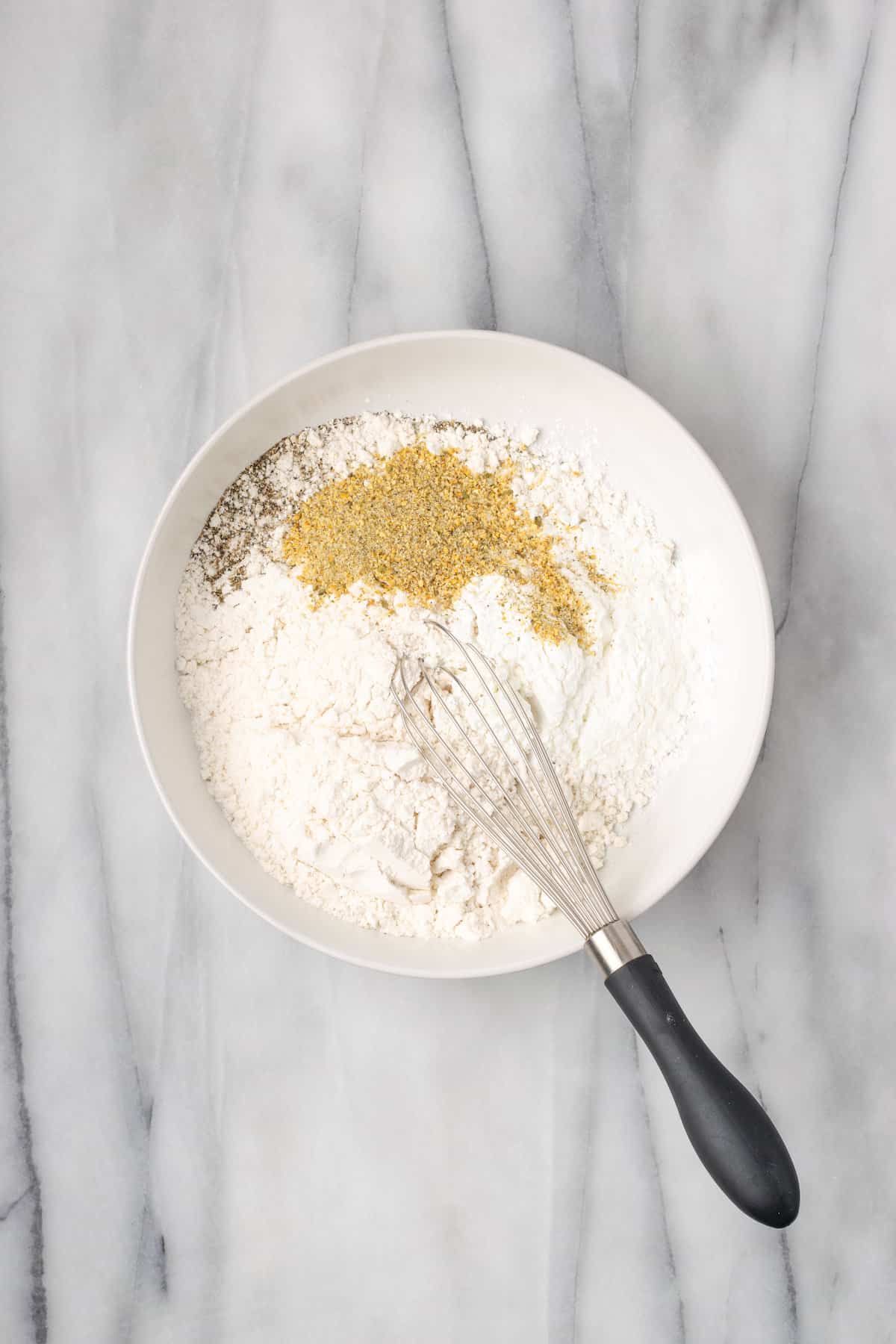 Seasoned flour is whisked together in a white bowl.